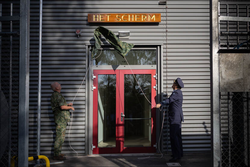 2 militairen trekken een zeil weg van het naambord 'Het Scherm'