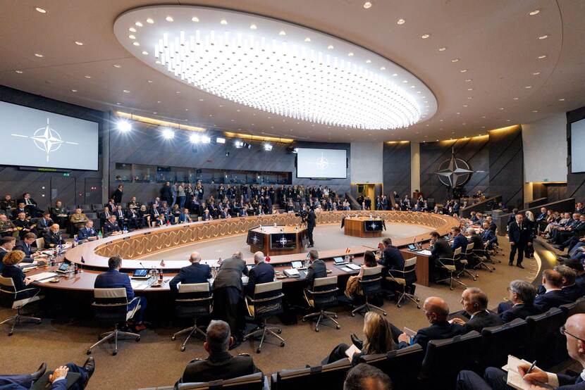 Ovale zaal met sprekers in pak uit uiteenlopende landen.