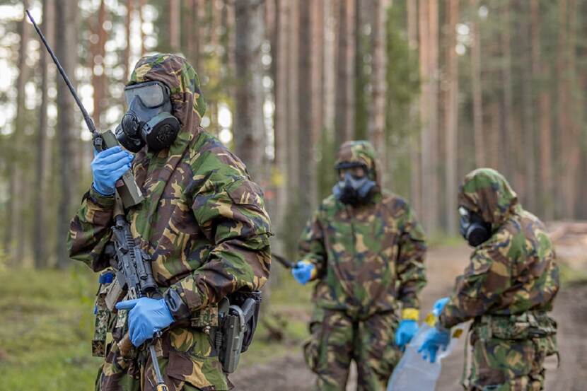 Drie militairen met gasmaskers op in bos bij oefening in Litouwen