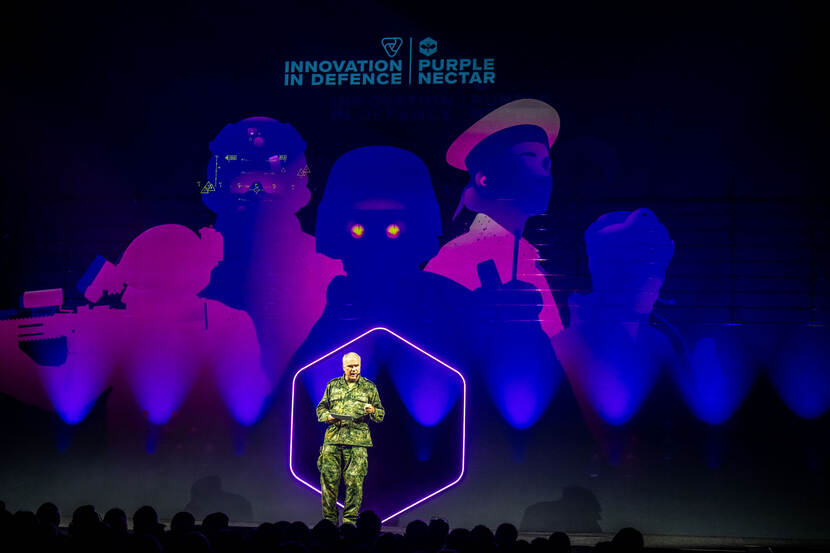 Generaal Onno Eichelsheim op podium tegen paarsblauwe achtergrond.