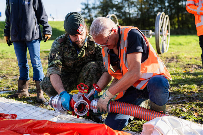 Een waterschapsmedewerker en een militair werken tijdens een oefening zij aan zij tijdens een noodsituatie door watersnood.