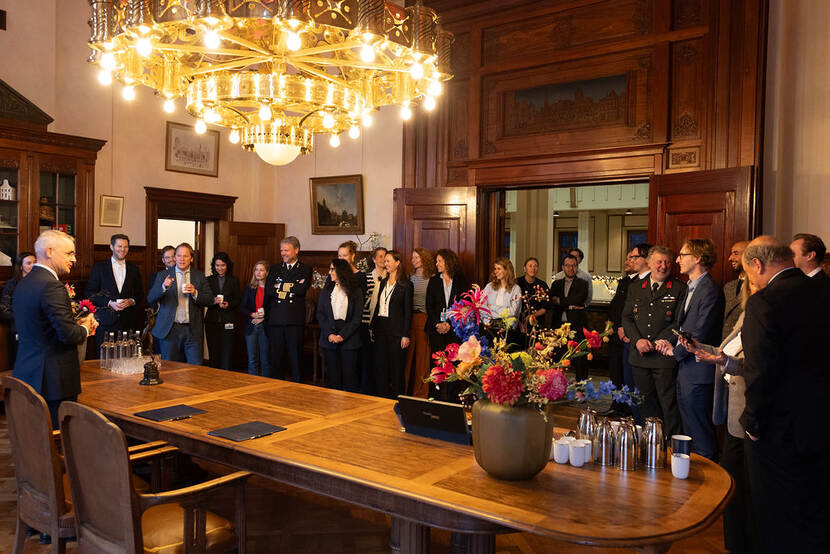 Mensen om een ingelegde houten tafel met een goudkleurige kroonluchter erboven.