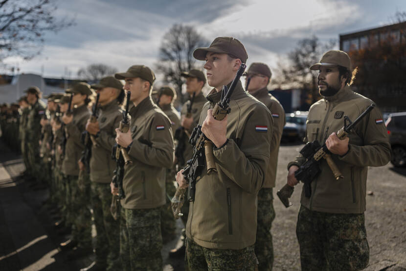 2 rijen jonge mensen met geweer in de hand en petje op.