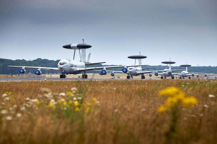 4 Awacs-toestellen achter elkaar op de grond met bloemetjes op de voorgrond.