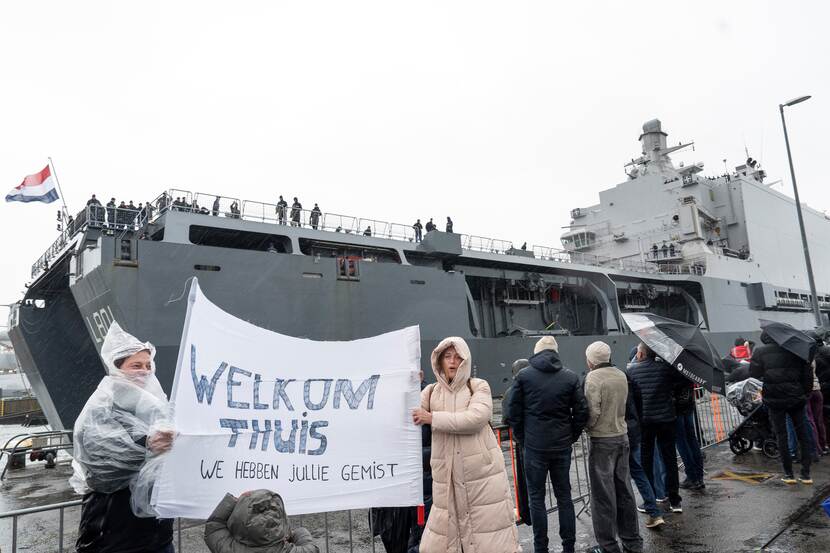 Twee mensen houden spandoek met Welkom Thuis vast bij aankomst marineschip.