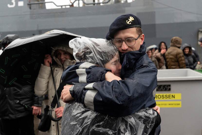 Militair omhelst vrouw in regenkleding innig.