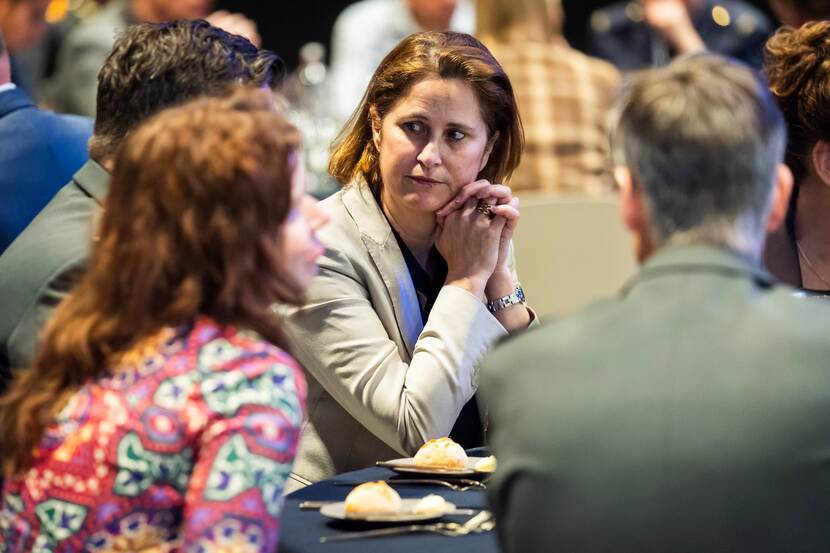 Mensen aan een tafel, waarvan 1 vrouw prominent in beeld.