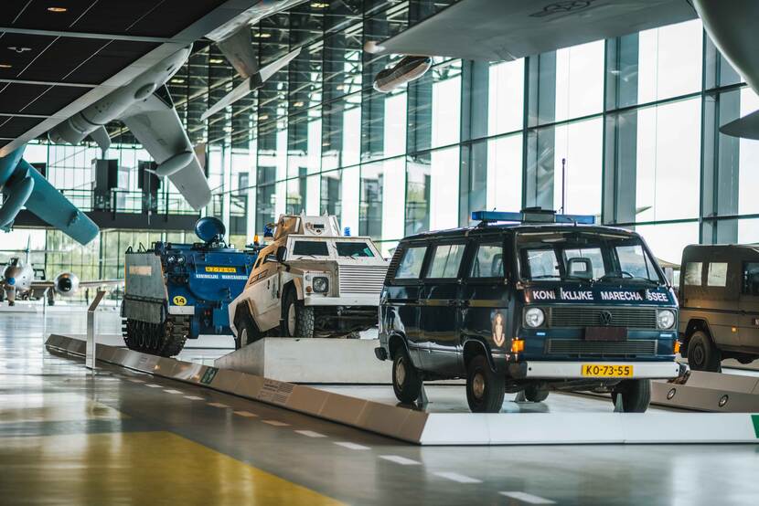 Museumvloer met militaire vliegtuigen, een busje en een rupsvoertuig.