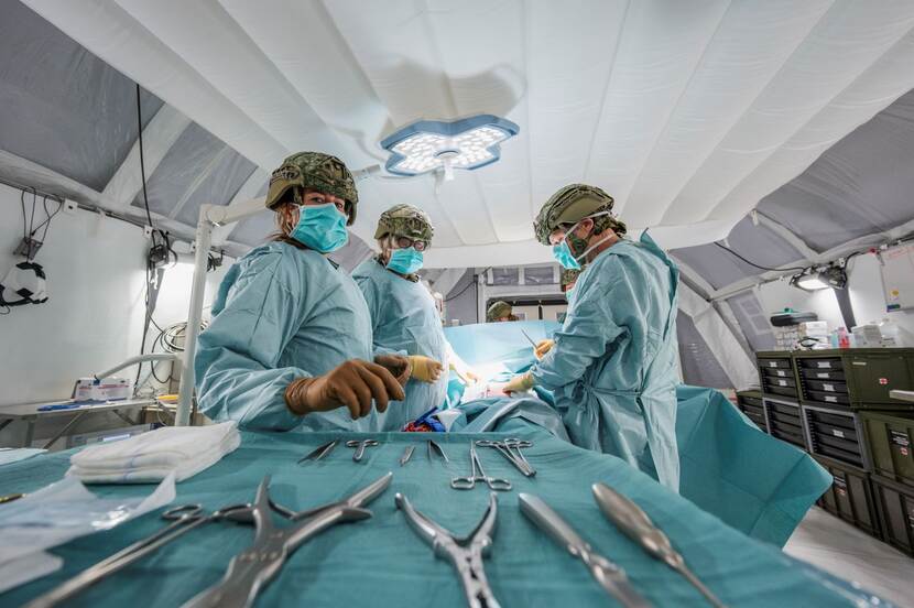 Gehelmd medisch team aan het opereren in groene pakken met zilverkleurige instrumenten op een tafel op de voorgrond uitgestald.