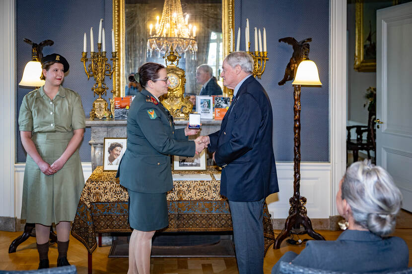 Militair overhandigt nabestaande onderscheiding.