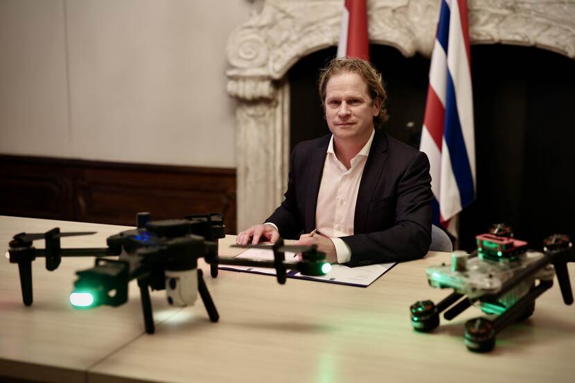 De staatssecretaris tekent het contract. Voor hem op de tafel staan 2 drones.