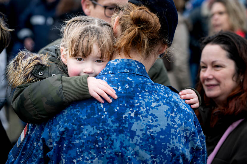 Een jong meisje kijkt over de schouder van een vrouwelijk marinier met staartje die op de rug zichtbaar is. Rechts een vrouw.