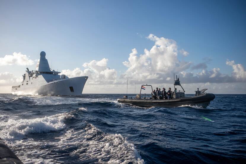 Een aantal mannen vaart op een boot voor een marineschip uit.