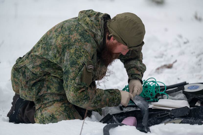 Militair op knieen in de sneeuw bezig met bevestiging van draden.