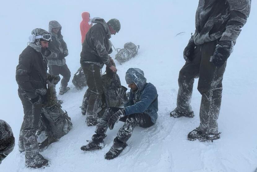 Mariniers staan in de sneeuw om een man heen die op de grond zit en uit een beker drinkt.