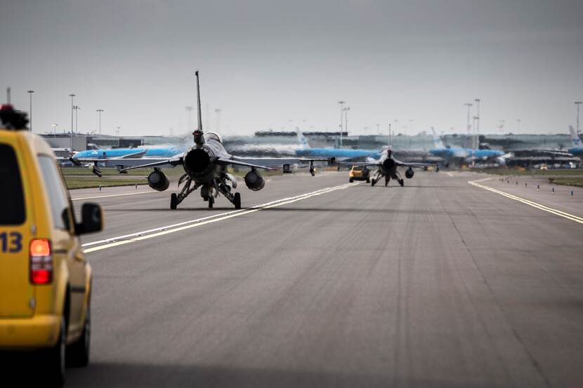 2 F-35's gezien van de achterzijde. Linksvoor een gele auto. Op de achtergrond KLM-toestellen