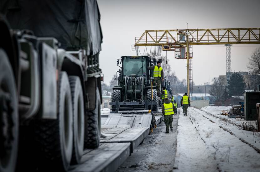 Militaire voertuigen op rails. Militairen in gele hesjes bezig met lossen.