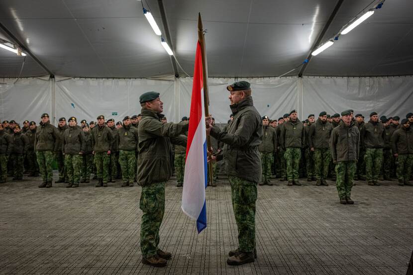 2 militairen staan tegenover elkaar en houden Nederlandse vlag vast.
