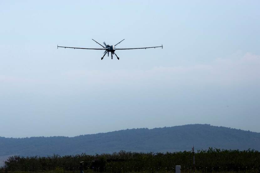 MQ9 Reaper in de lucht boven heuvelachtig landschap.