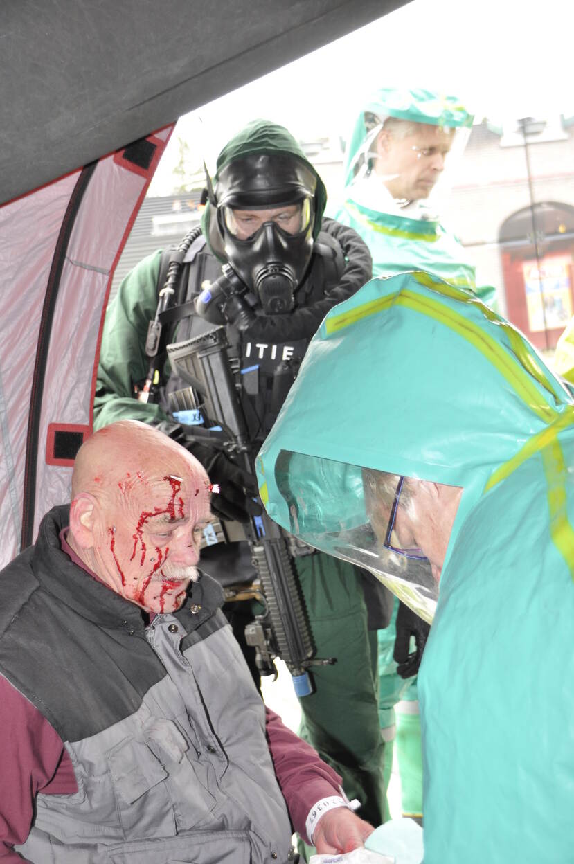Gewonde man wordt verzorgd door een persoon in een beschermend pak.