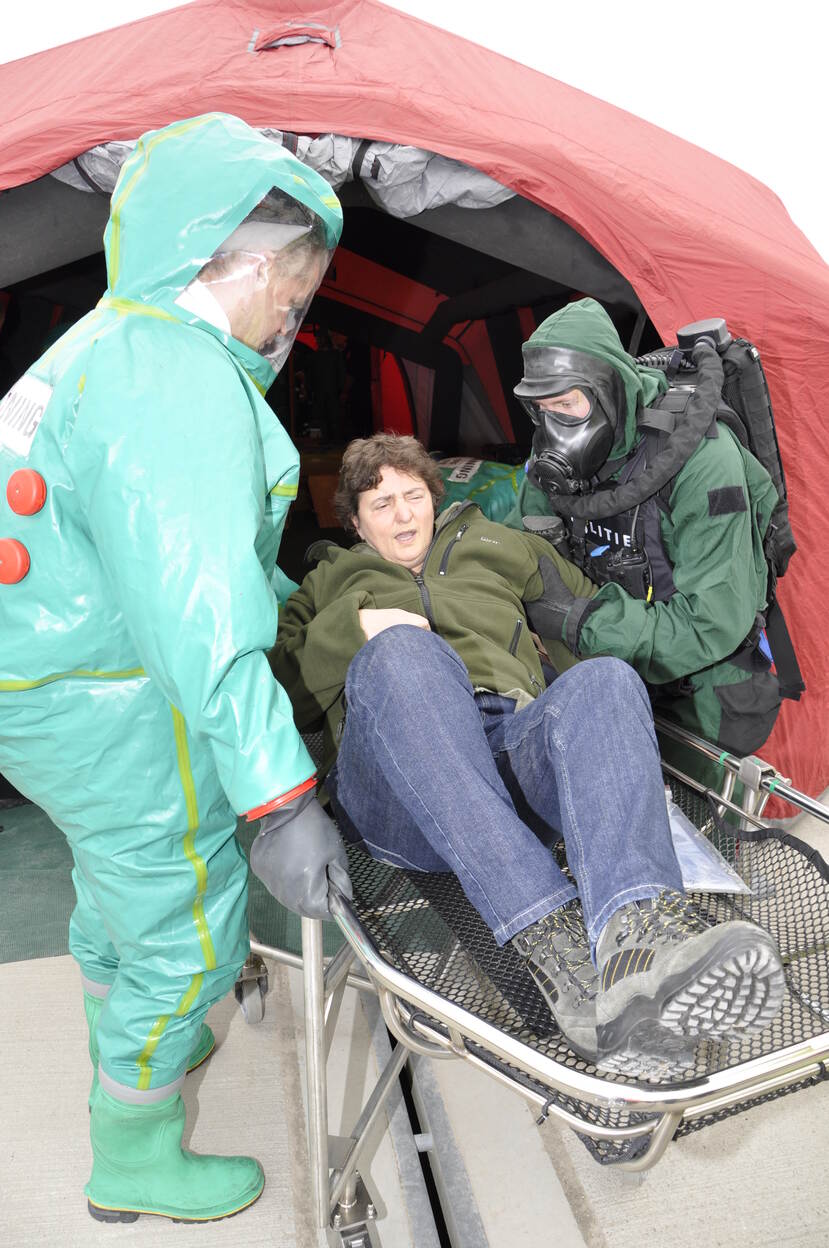 Vrouw wordt op een brancard een tent in gedragen door personen in beschermende pakken.