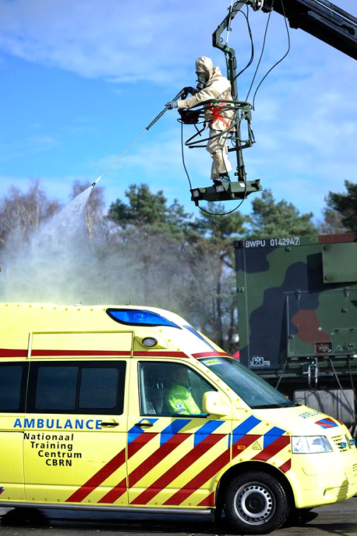 Persoon in beschermend pak spuit vanaf een kraan een ambulance schoon.