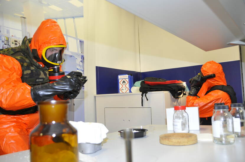 Personen in beschermende oranje pakken doen een analyse in een lab.