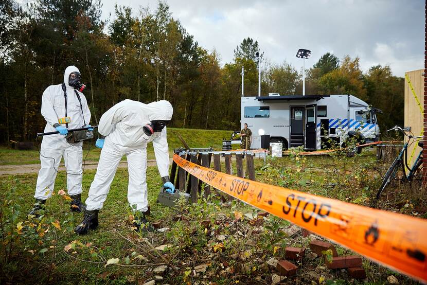 2 personen in beschermende pakken voeren een meting uit op een veld.