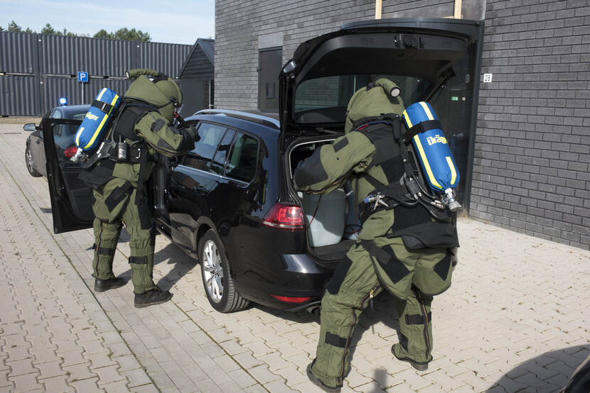 Militairen in beschermende pakken onderzoeken een auto.