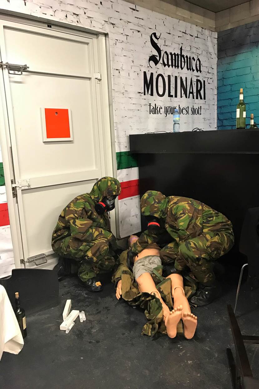 2 militairen met beschermend masker onderzoeken een gewonde in een Italiaans restaurant.