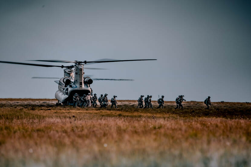 Een Chinook-helikopter op de grond. Landmachtmilitairen komen uit de laadruimte.