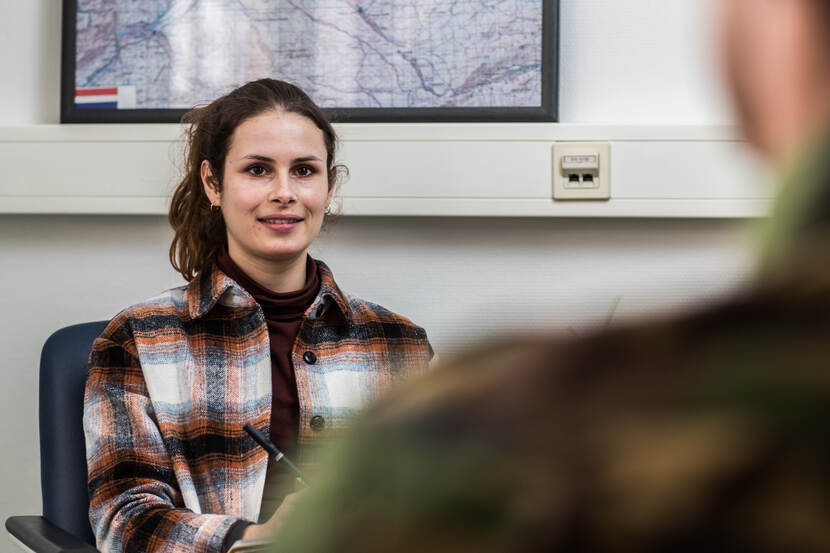 Een vrouw zit in een kamer en kijkt naar een militair.