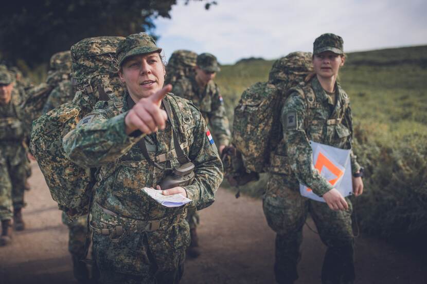 Militairen met rugzakken navigeren lopend met kaart.