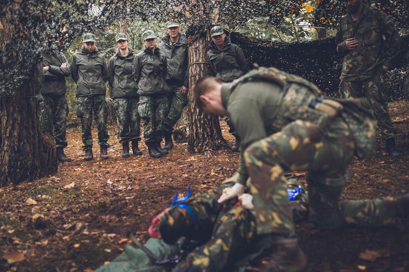 Militairen kijken hoe collega voordoet hoe je een tourniquet aanlegt.