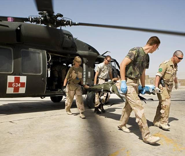 Militairen vervoeren per brancard een patiënt uit een helikopter.