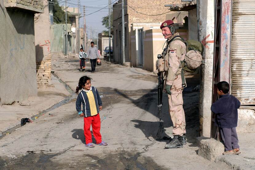 Infanterist lacht bij een klein meisje op straat in Irak.