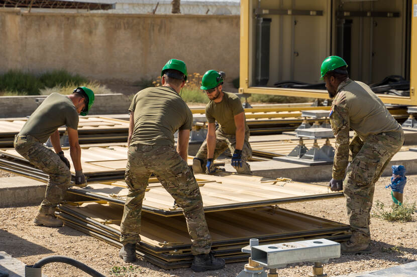 4 militairen tillen samen de wand van een container.