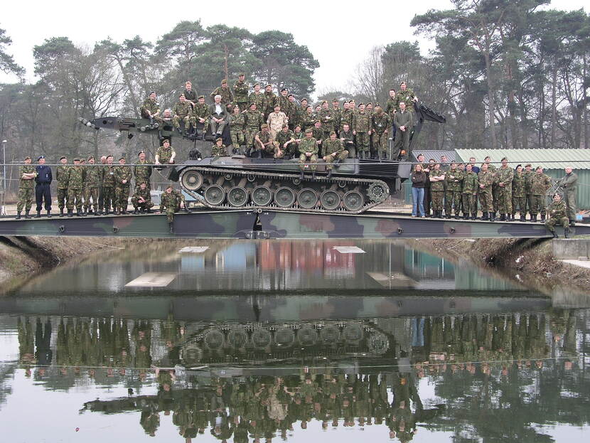 Een grote groep militairen zitten voor de foto op een tank.