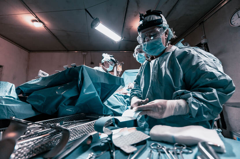 Een arts in groene operatiekleding knipt een verband.