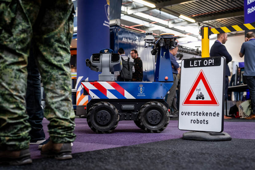 Een onbemand voertuig rijdt over een beursvloer met op de voorgrond een waarschuwingsbord.