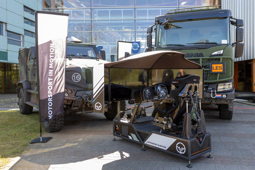 Een race-simulator met op de achtergrond 2 legervoertuigen.