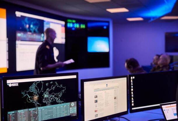 Computers in een donkere ruimte met wazige mensen op de achtergrond.