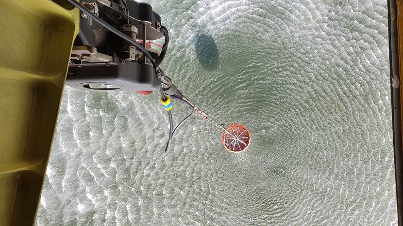Een bambi bucket wordt in open water gevuld terwijl het onder een Chinook hangt.