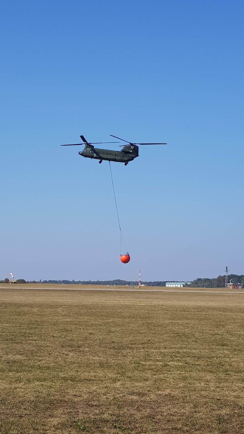 Een Chinook in de lucht met de nieuwe bambi bucket eronder.