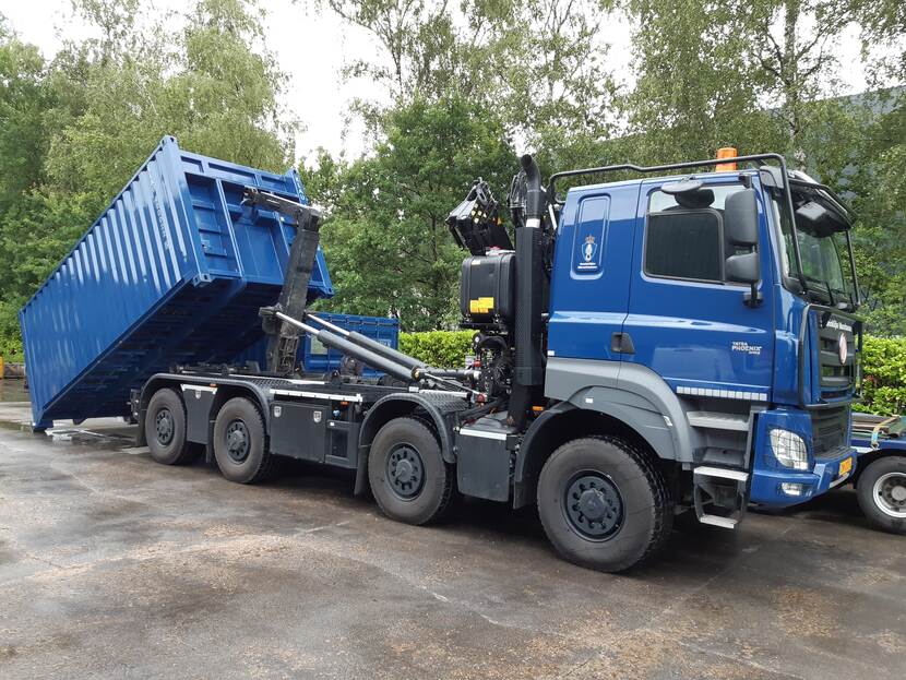 Vrachtauto met wissellaadsysteem en autolaadkraan zet container neer.