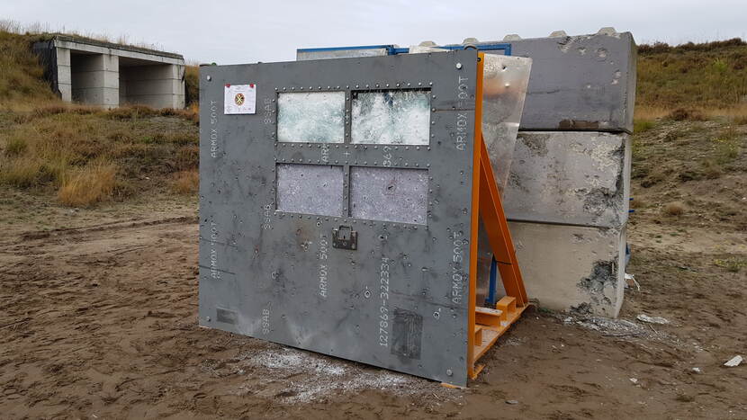 Een stuk beschadigd pantserstaal met pantserglasramen buiten op een testbaan voor blokken beton.