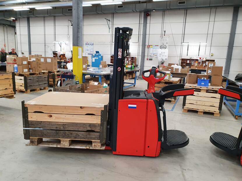 Rode stapelaar met een palletbox op de vorken in een magazijn.