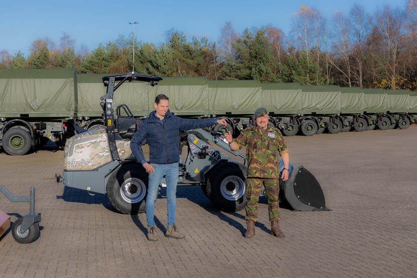 Sleuteloverdracht tussen burger en militair voor een wiellaadschop op een parkeerplaats met aanhangwagens.