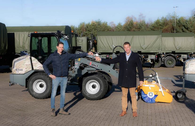 Sleuteloverdracht tussen burger en militair voor een wiellaadschop op een parkeerplaats met aanhangwagens.