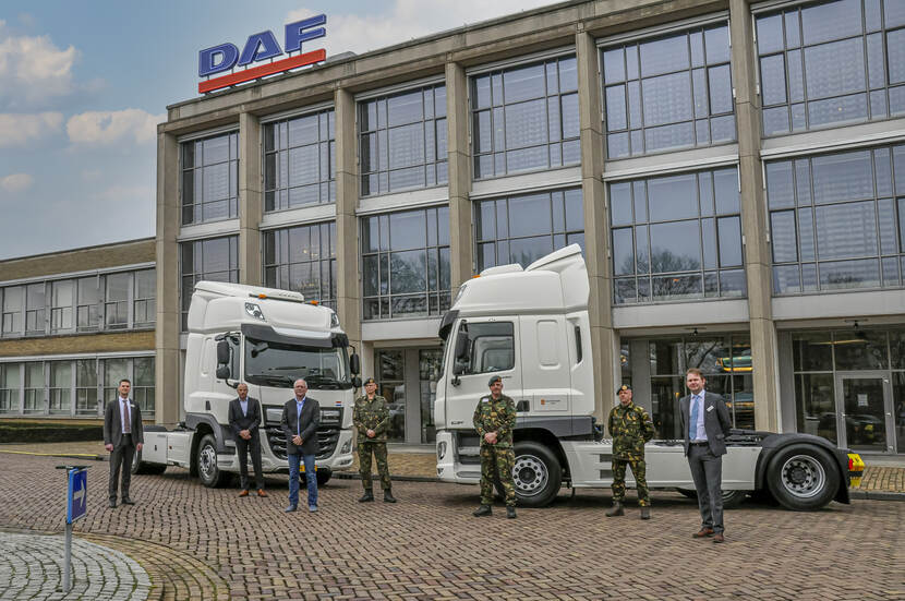 Militairen en burgers met 2 vrachtvoertuigen van de Witte Vloot voor het kantoor van DAF waar de vrachtvoertuigen zijn gekocht.
